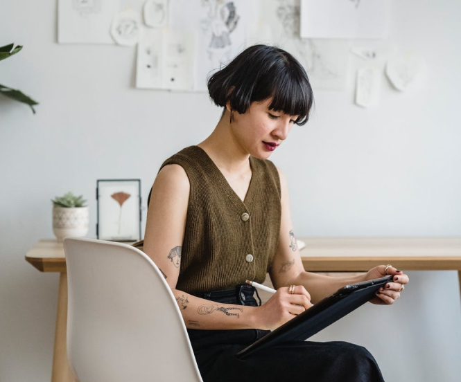 a woman writing on a tablet PC sitting on a chair in a well lit room