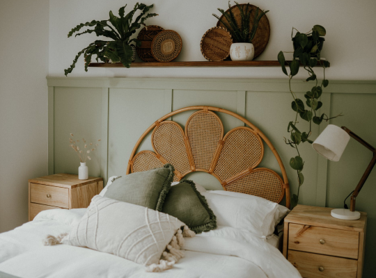 a cozy bed with 2 side tables, some pillows and some plants